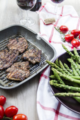 Grilled lamb with green asparagus, grill pan, red vine, wood background.