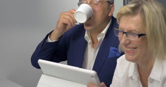 Senior man and woman in glasses talking on business and using tablet computer. They have positive and constructive conversation