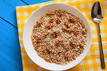 Dry oatmeal flakes  with walnuts in a white plate on a blue wood