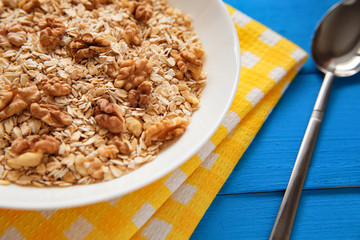 Dry oatmeal flakes  with walnuts in a white plate on a blue wood