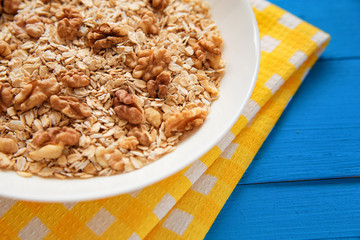 Dry oatmeal flakes  with walnuts in a white plate on a blue wood