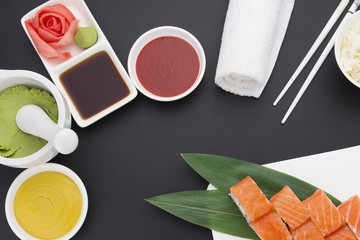 Japanese cuisine. Salmon sushi on a wooden plate with ginger wasabi and sauces over black background
