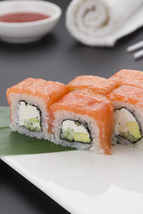 Japanese cuisine. Salmon sushi on a wooden plate with ginger wasabi and sauces over black background