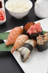 Japanese cuisine. Sushi nigiri set on a white plate with ginger wasabi and different sauces over black background