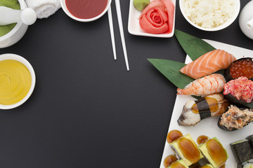 Japanese cuisine. Sushi nigiri set on a white plate with ginger wasabi and different sauces over black background