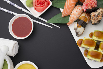 Japanese cuisine. Sushi nigiri set on a white plate with ginger wasabi and different sauces over black background