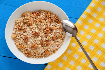 Dry oatmeal flakes  with walnuts in a white plate on a blue wood