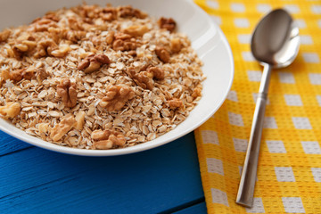 Dry oatmeal flakes with walnuts in a white plate on a blue wooden table, the decor of the napkin. Oatmeal with nuts. Top view point.