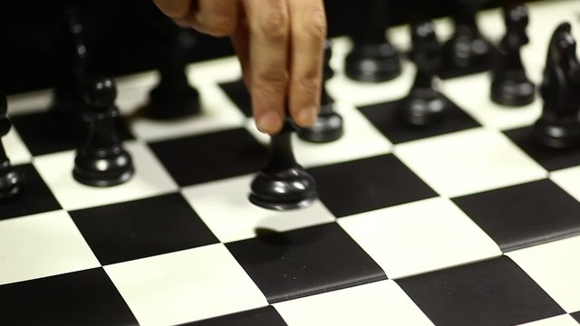 Arrangement of black chess pieces on chess board, with pawn moving.