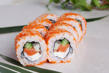 roll with tobiko orange, salmon, cucumber shrimp and sweet red peppers on a tropical leaf close-up menu isolated