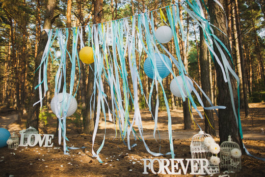Beautiful place for outside wedding ceremony in wood. Wedding settings. Festive stylish decorations made by blue and white Japanese lanterns and many ribbons. Horizontal image.