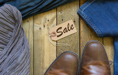 Sale Schild auf rustikalem Hintergrund mit Schuhen, Stoff und Jeans