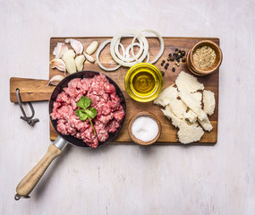 ingredients for hamburgers, minced meat in a frying pan with pepper and onion rings on a cutting board on wooden rustic background top view