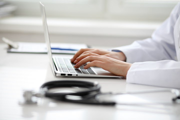 Female doctor typing on laptop, close up