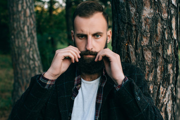 Portrait brutal bearded hipster man in the forest and He twists his mustache