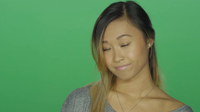 Cute Asian girl looking sad and then smiling, on a green screen studio background