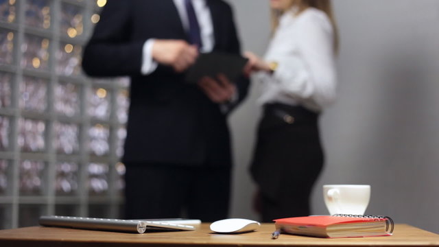 Documents on office table and man and woman talking in the background