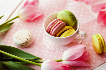 A beautiful flowers pink tulips with colorful macaroons laid in cup on white wooden background with pink Lacy napkin