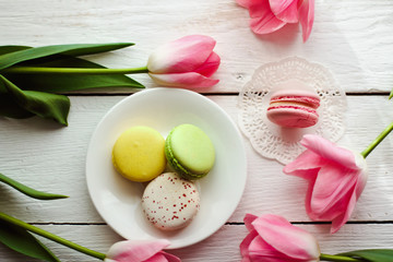 A beautiful flowers pink tulips with colorful macaroons laid on a white platter on white wooden background