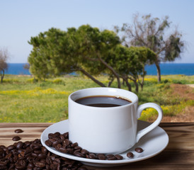 Coffee beans and coffee in white cup on wooden table opposite a