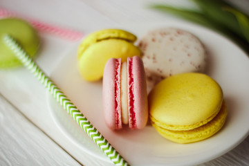 A beautiful flowers pink tulips with colorful macaroons laid on a white platter on white wooden background