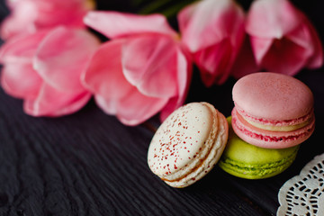 A beautiful flowers pink tulips with colorful macaroons laid on dark wooden background with Lacy napkin