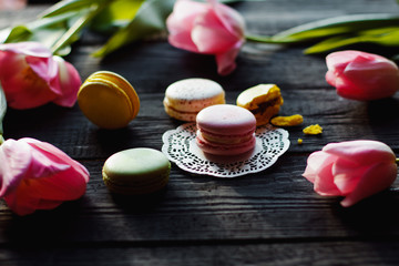 A beautiful flowers pink tulips with colorful macaroons laid on dark wooden background with Lacy napkin