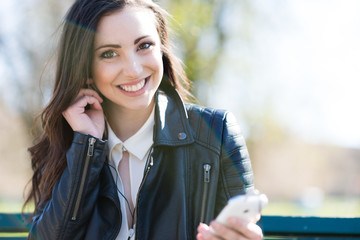 Smiling young woman using earphones attached to a mobile phone