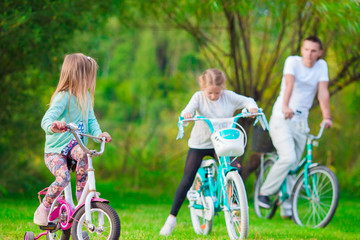 Family of young father and little kids biking at summer warm day