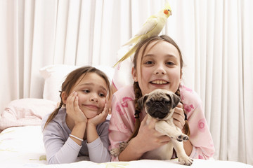Mixed race girls with dog and bird on bed