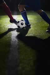 Two soccer players kicking a soccer ball