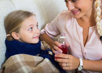 Unwell little girl taking mixture from worried mother