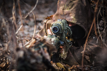 Sniper wearing camouflage suit with rifle hide in the woods