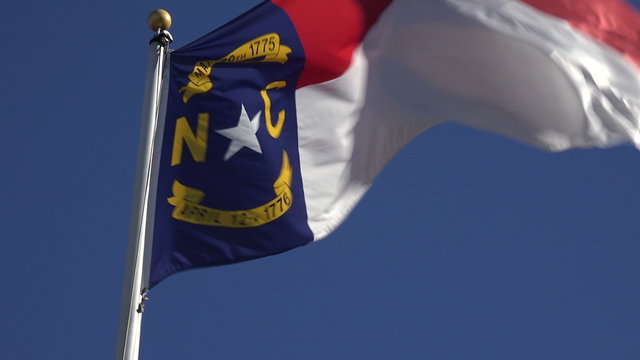 North Carolina flag in wind with blue sky background, NC, USA