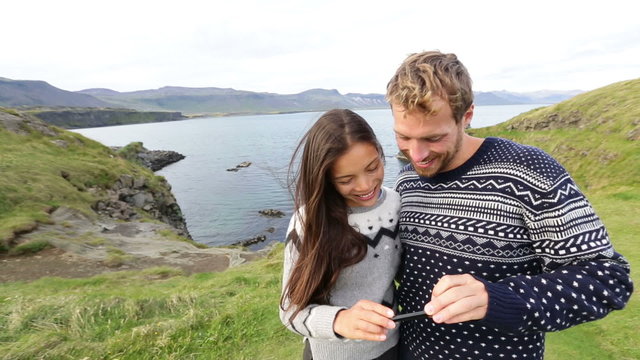 Couple on using smartphone app on Iceland. Happy couple using travel apps or map on smart mobile cell phone sightseeing visiting Arnarstapi, Snaefellsnes, Iceland.