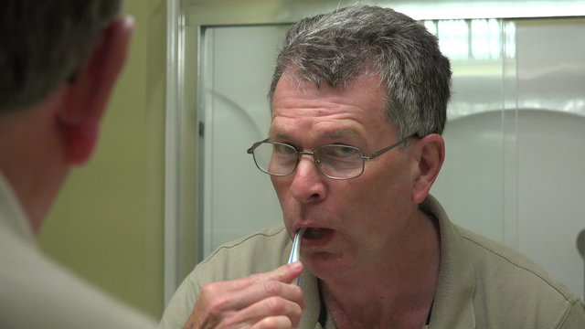 Senior man brushes teeth in bathroom
