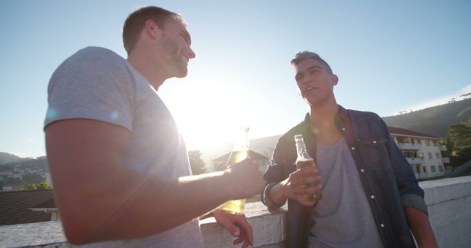 Two friends drinking and laughing on the rooftop at sunset