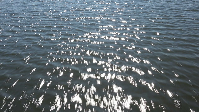 Fly low over water, sun glints in water
