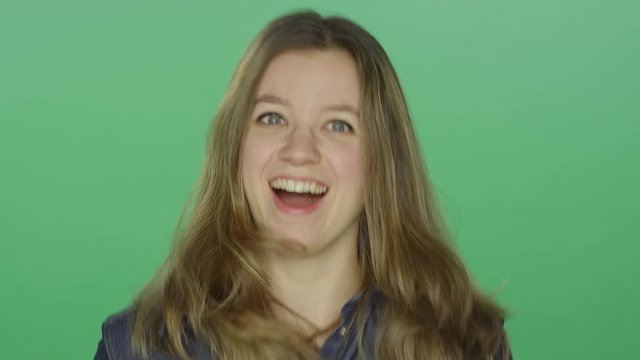Young woman looking pleasantly surprised, on a green screen studio background