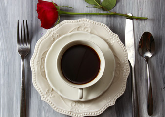 Overhead view of a coffee cup and plate with black coffee and a red Rose.