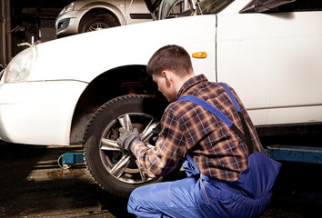 Car mechanic screwing or unscrewing car wheel of lifted automobi