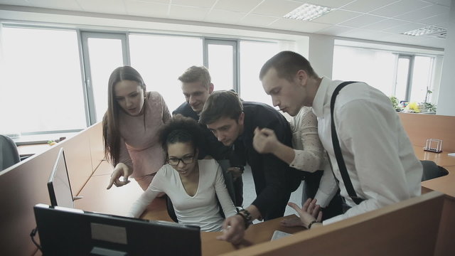 Group of multiethnic office workers around colleague using computer