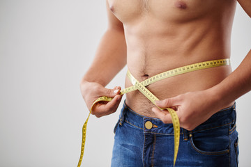 Cropped image on man measuring his waist with tape