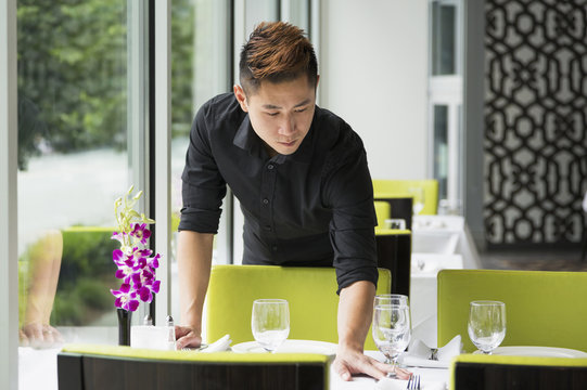 Asian Waiter Setting Table In Restaurant