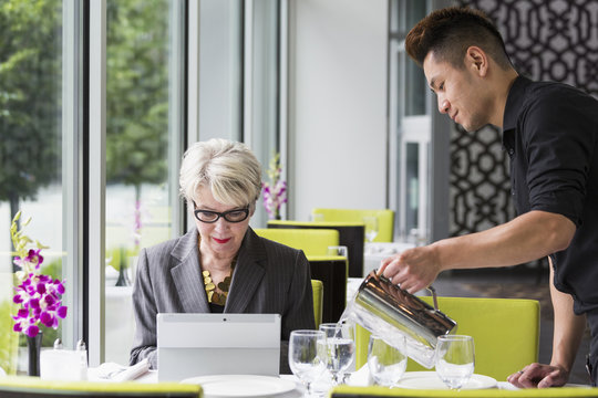 Waiter pouring water for customer in restaurant