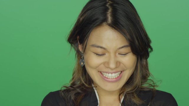 Young Asian woman smiling and laughing, on a green screen studio background