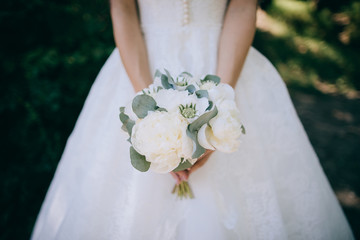 Bride in a white dress holding a beautiful Eucalyptus white peonies wedding bouquet in her hands