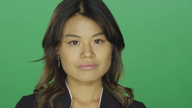 Young Asian woman crossing her arms and looking upset, on a green screen studio background