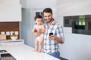 Father using mobile phone while holding baby boy