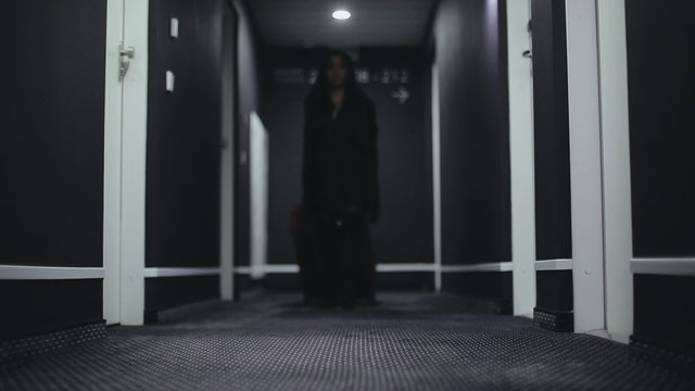 Asian woman in a long corridor of the hotel with a large red suitcase